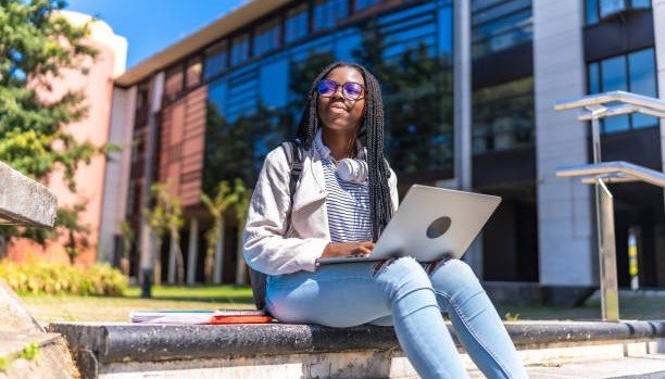 Student sitting outside a university building working on a laptop