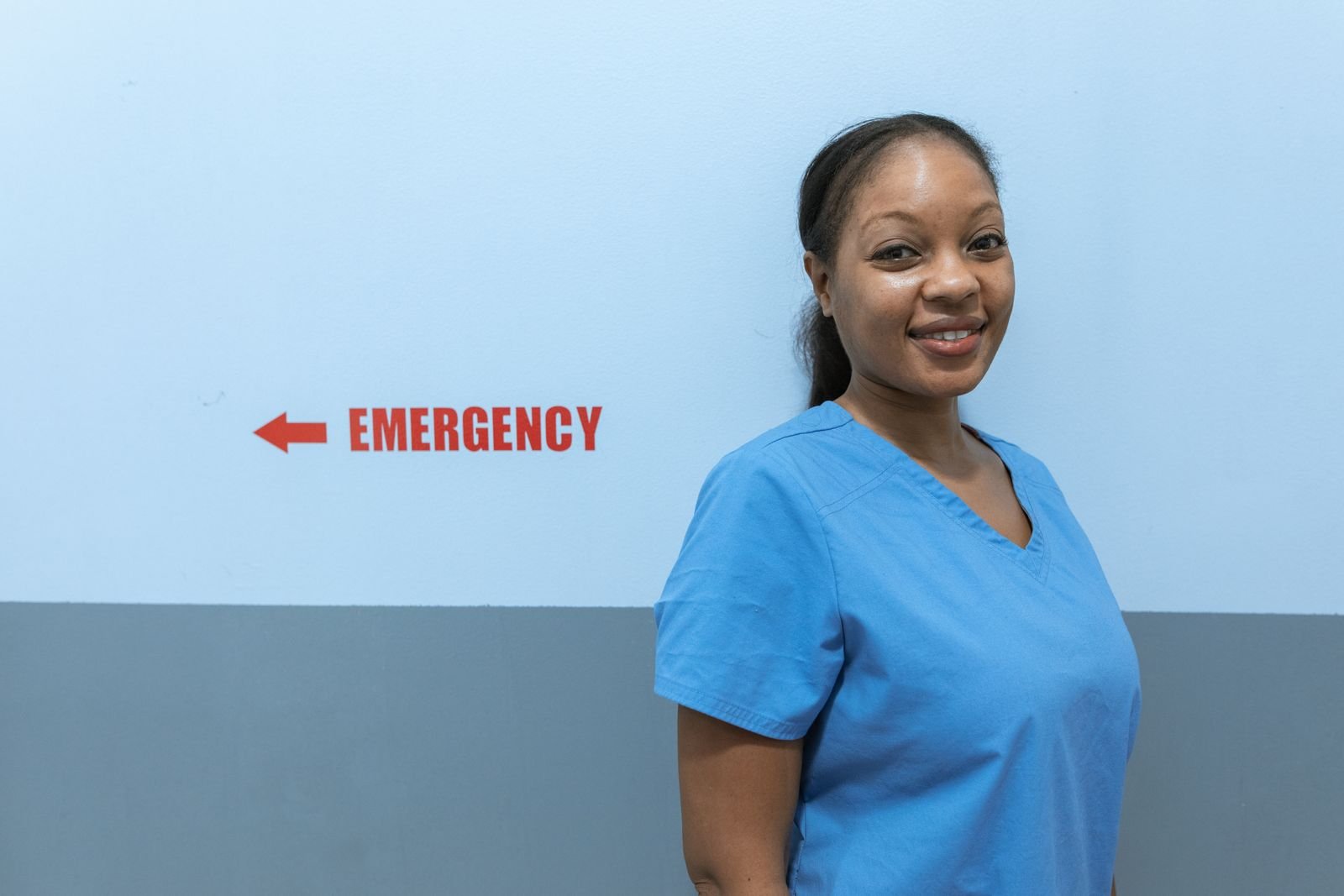 South African nurse in scrubs standing near a hospital emergency department sign